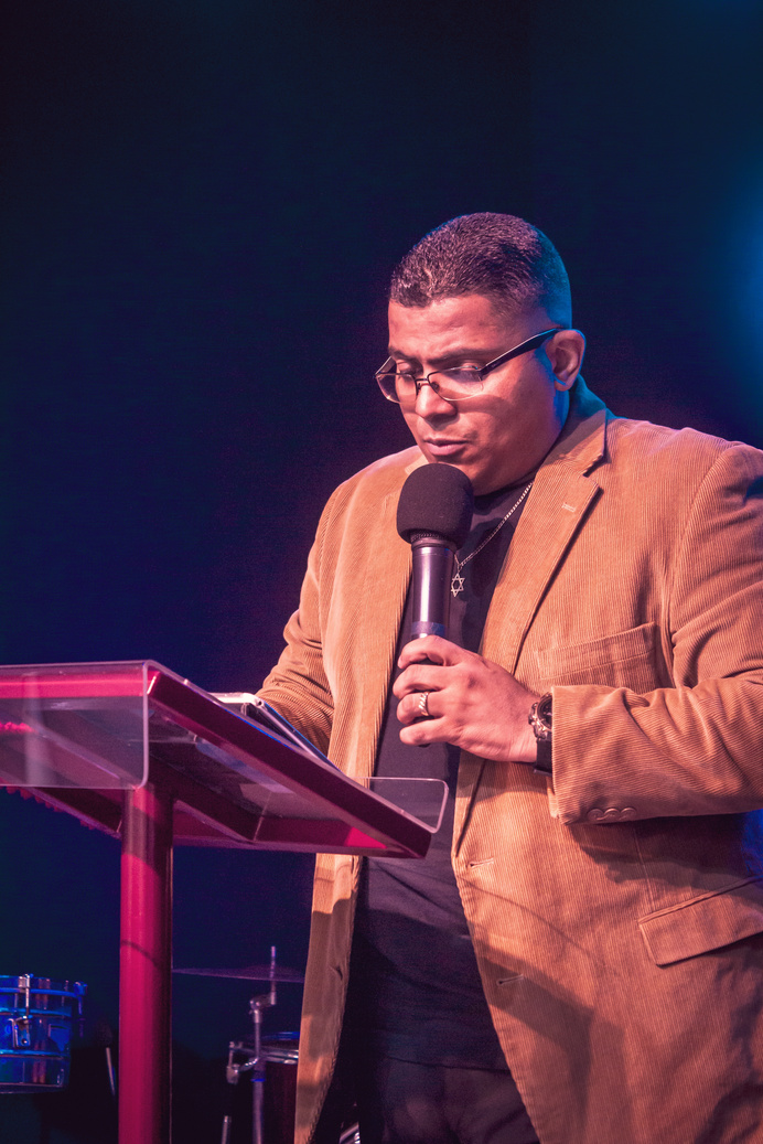 Man in a Brown Blazer Reading while Holding a Microphone